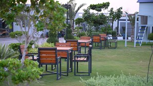 An outdoor seating area with wooden tables and chairs, surrounded by greenery and a playground structure. - The Most Luxurious Private Resort in Karachi (Karachi)