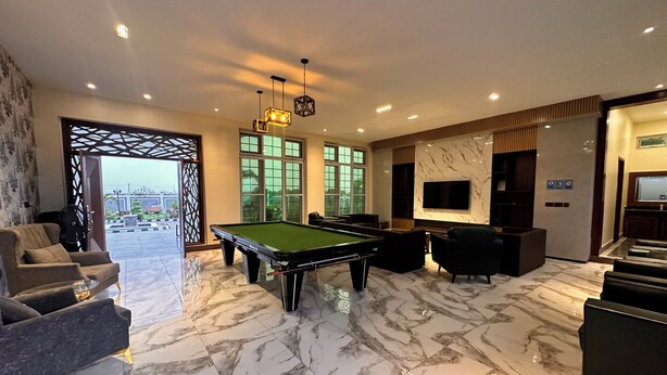 A modern indoor space with a pool table, comfortable seating, a TV, and a view through large windows. - The Most Luxurious Private Resort in Karachi (Karachi)