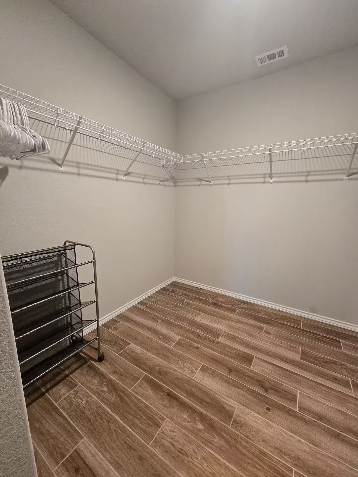A closet with a metal rack and a black rack, wooden flooring, and a white wall.