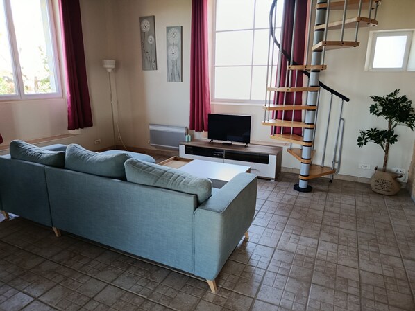 A living room with a sofa, TV, staircase, and a potted plant. - "La Borie" charming gîte with swimming pool in Daglan at Mas de Cause (Daglan)