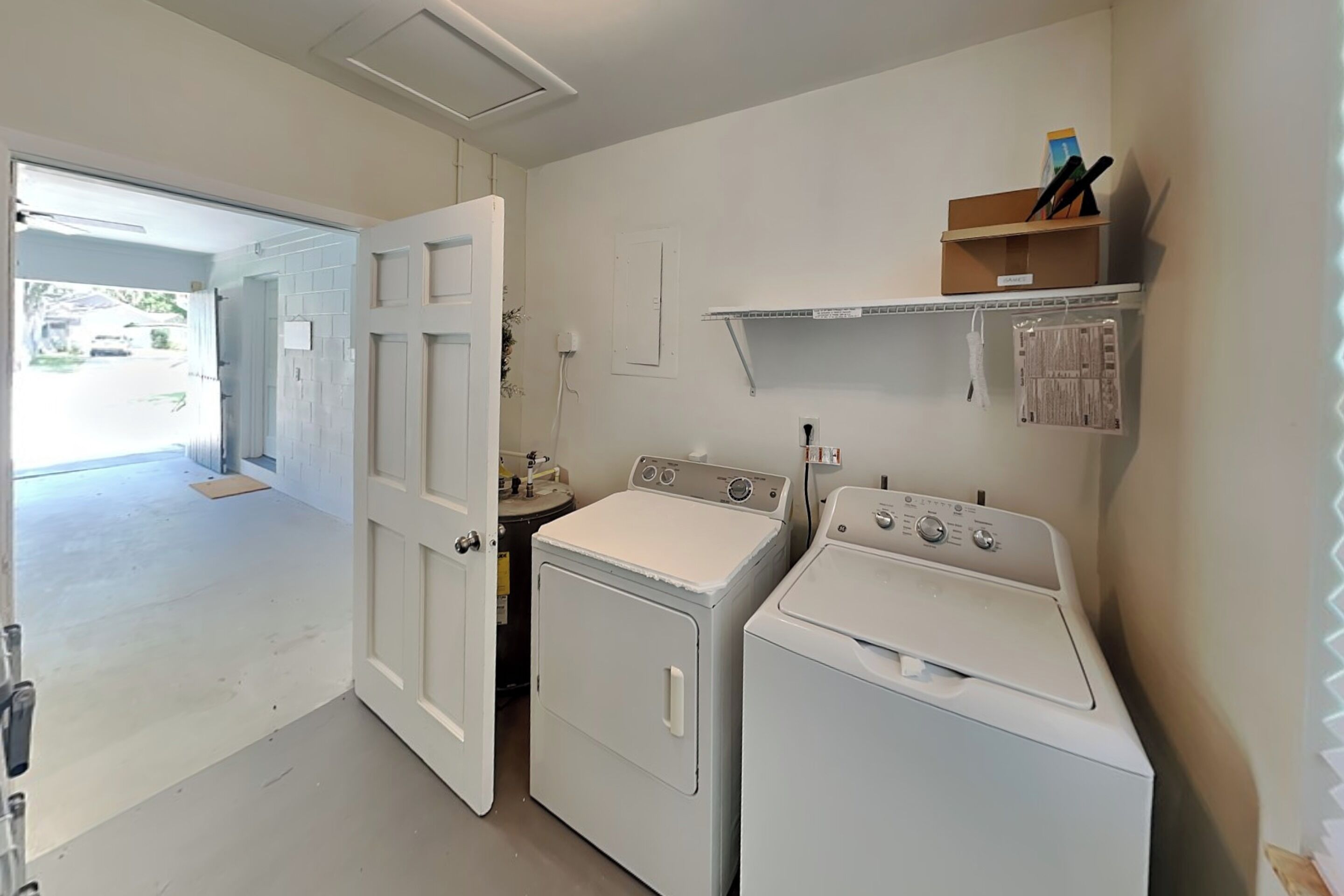 A laundry room with two washing machines, a dryer, and a shelf with cleaning supplies.