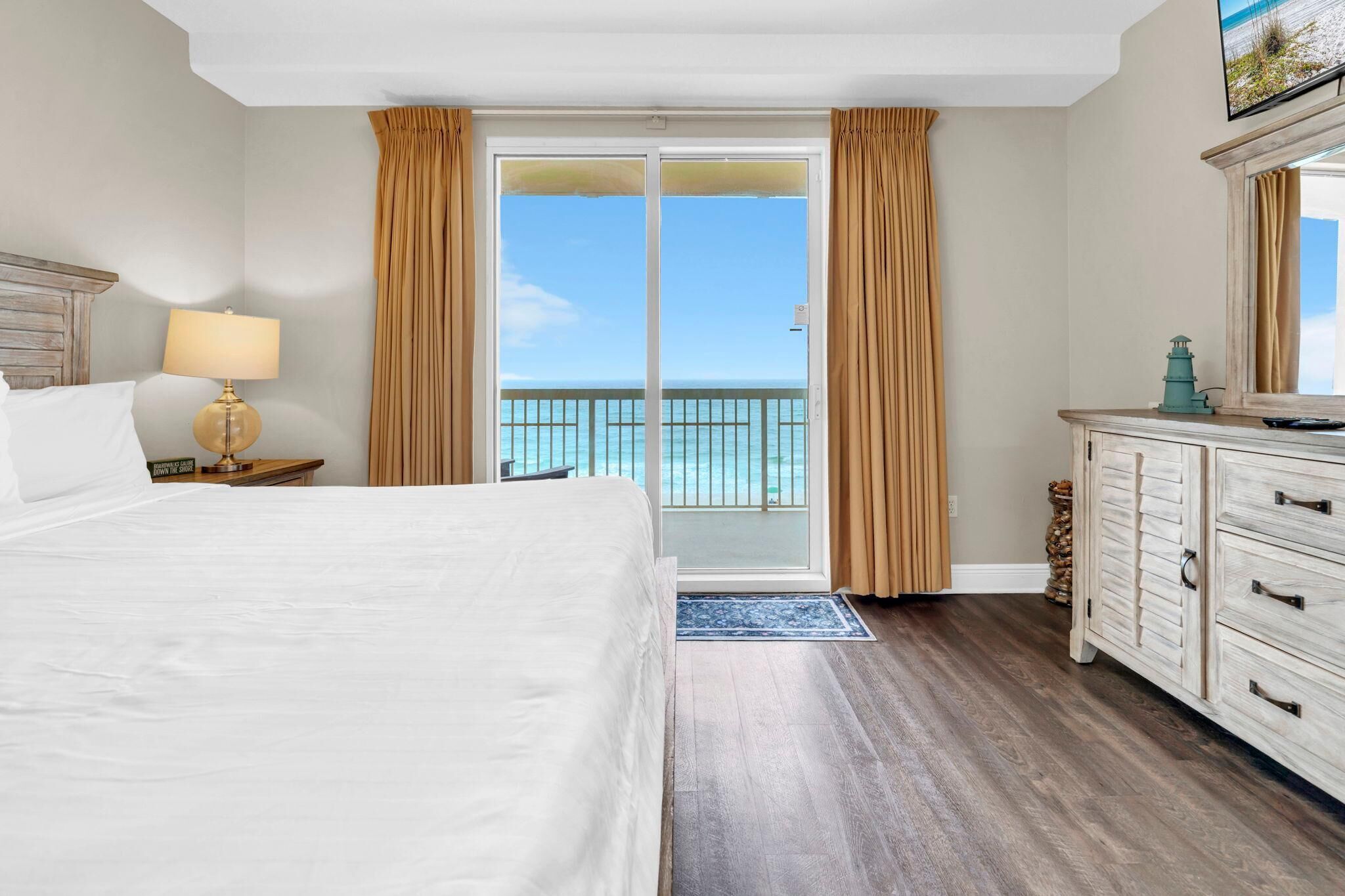 Une chambre d’hôtel comprenant un lit, une table de chevet avec une lampe, une commode, un téléviseur et un balcon avec vue sur l’océan.