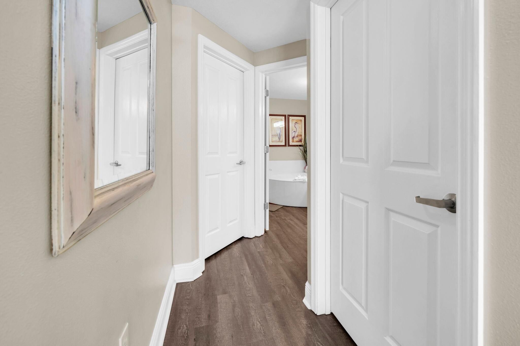 A hallway with white doors, a mirror, and a wooden floor.
