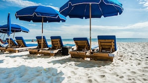 A beach with rows of wooden lounge chairs and blue umbrellas. - Celadon 409- Champagne Sunsets (Panama City Beach)
