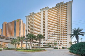 A high-rise hotel with multiple balconies, a covered walkway, and palm trees. - Celadon 409- Champagne Sunsets (Panama City Beach)