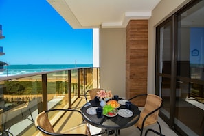 A balcony with a table set for two, overlooking a beach. - Duplex Vista Mar com Piscina Privativa  (Governador Celso Ramos)