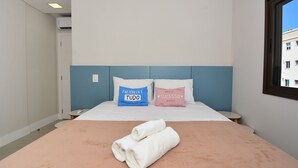 Ein Hotelzimmer mit einem Bett, zwei Kissen, einem Nachttisch und einem Fenster.