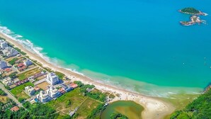 Eine Vogelperspektive einer Küstenregion mit Strand, einer kleinen Insel und einem Wohngebiet mit Gebäuden.
