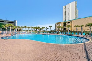 A swimming pool with lounge chairs and palm trees, surrounded by buildings. - Tidewater 13 (Panama City Beach)