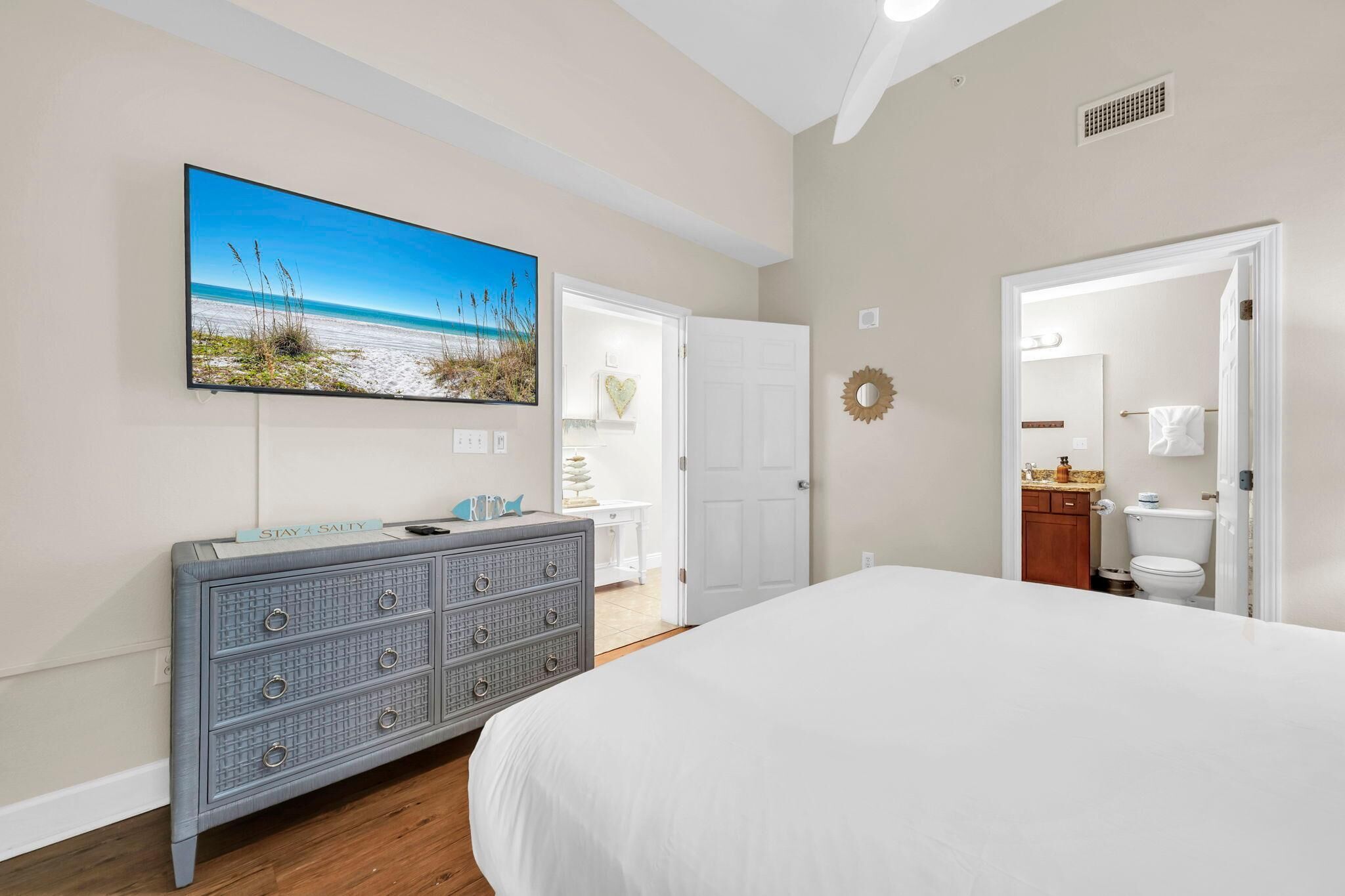 Un dormitorio con cama, cómoda, televisor y puerta que da a un baño.