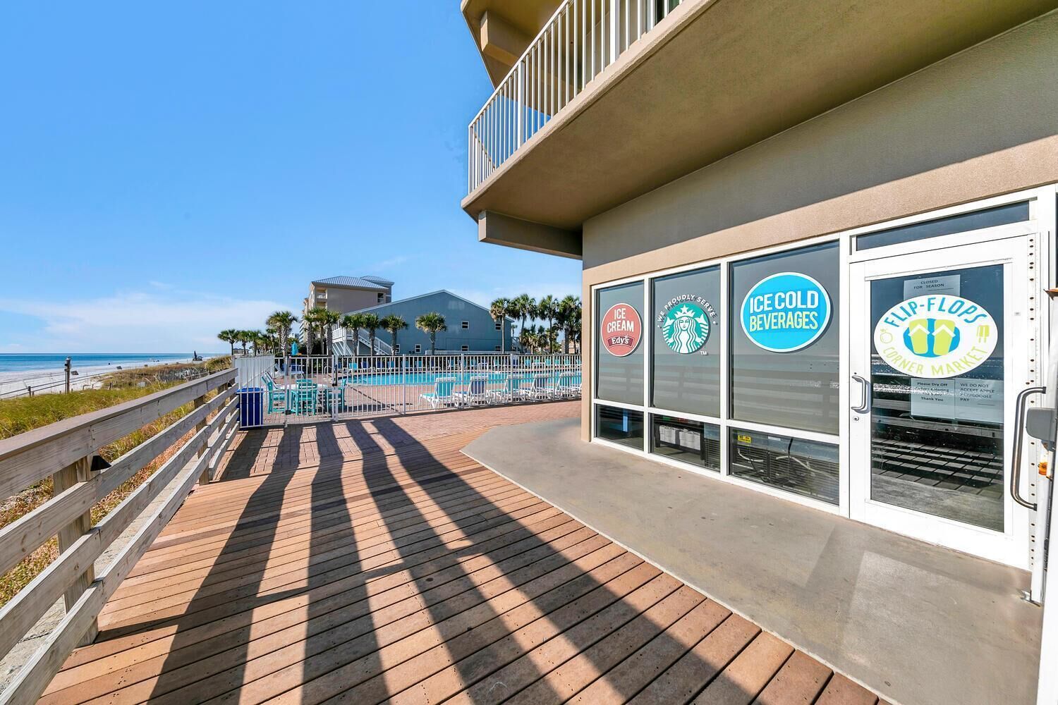 A beachside boardwalk with a pool area, a building with 'Ice Cold Beverages' and 'Ice Cream Edy's' signage, and a view of the ocean.