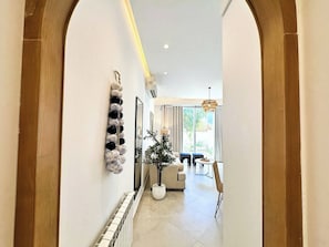 A hallway with a tiled floor, a radiator, a wall-mounted decorative item, and a view into a living area with a sofa, a table, and a plant. - Appartement Fella 2 Bedrooms (Sidi Bou Said)