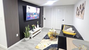 Un salon moderne avec un téléviseur à écran plat, un canapé noir, une table à manger et une plante en pot.