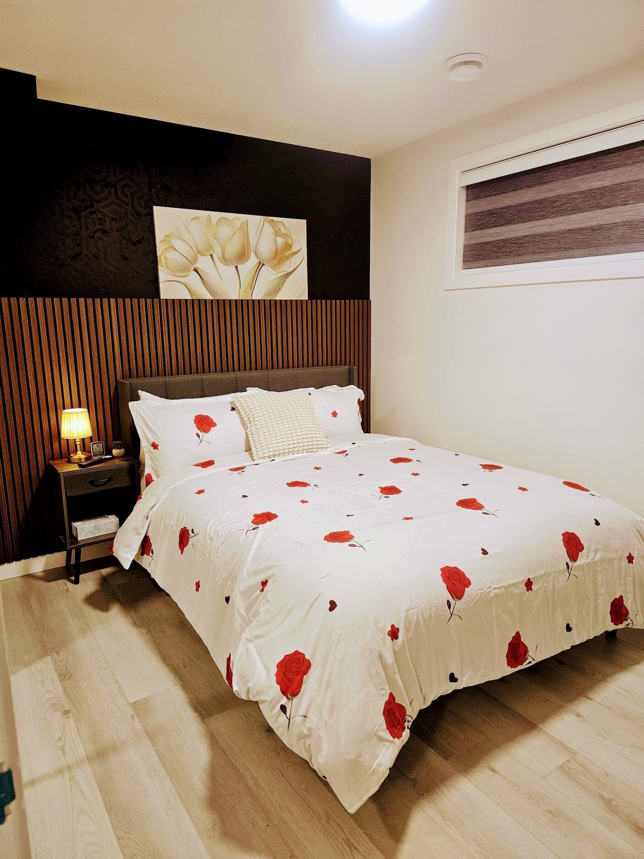 Une chambre à coucher avec un lit, une table de chevet, une lampe et un mur orné d’un tableau représentant des motifs floraux.