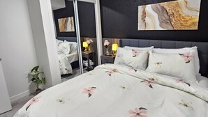 Une chambre à coucher comprenant un lit, une table de chevet, une lampe, un miroir et une œuvre d’art murale.