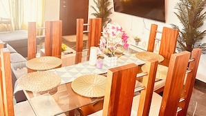 A dining area with a glass table, wooden chairs, woven placemats, a potted plant, and a large flat-screen TV mounted on the wall. - Niagara Beach Villa Your Private Caribbean Escape in Punta Cana (Punta Cana)