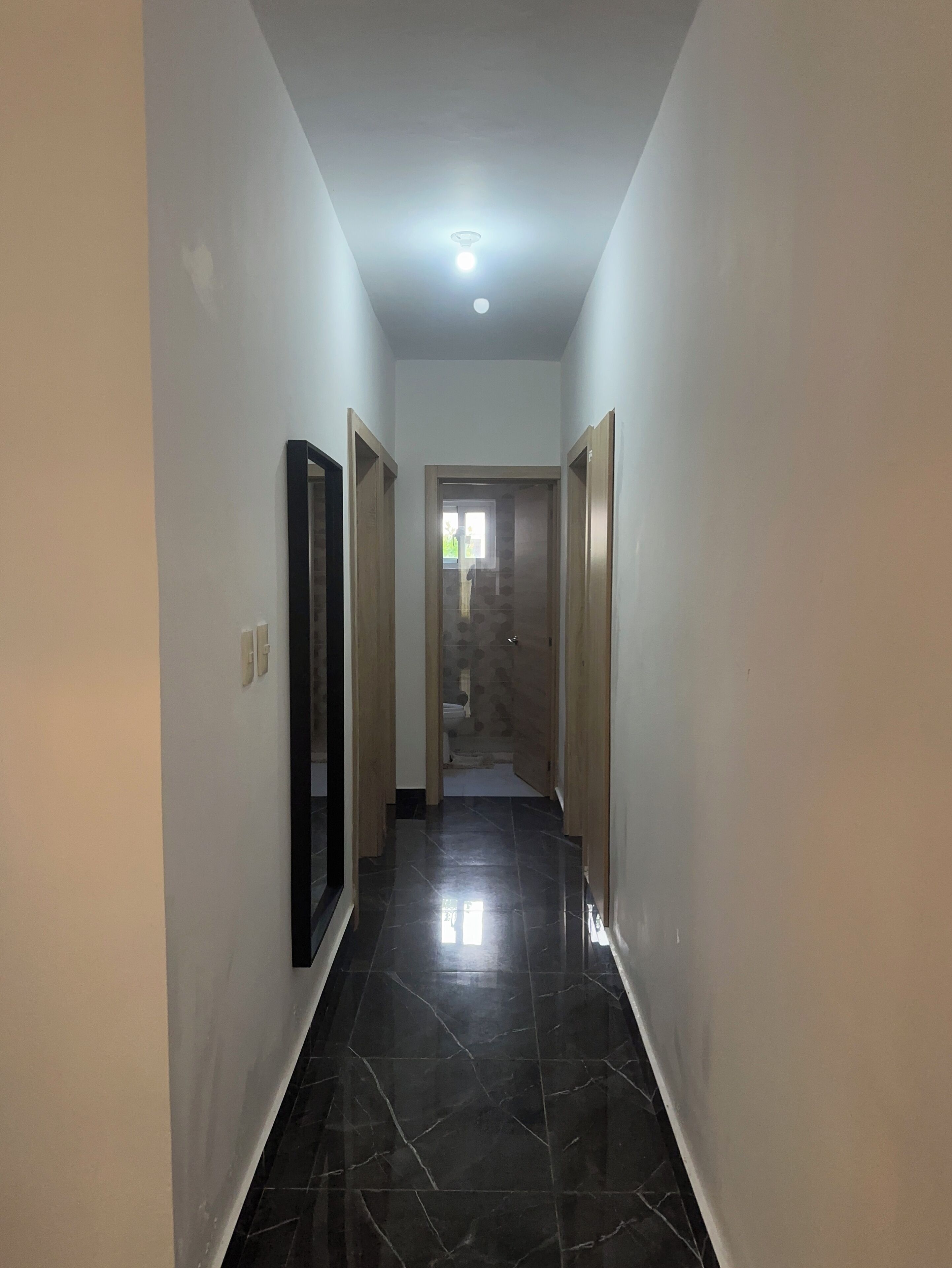 Un couloir avec un sol carrelé, un luminaire au plafond et des portes en bois.