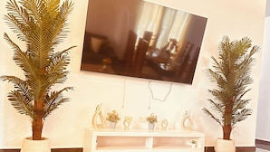 A living room with a flat-screen TV mounted on the wall, two potted plants, a white console table with decorative items, and a wooden coffee table. - Niagara Beach Villa Your Private Caribbean Escape in Punta Cana (Punta Cana)
