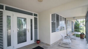 A covered outdoor area with a tiled floor, a black mat, white doors with glass panels, and a potted plant. - Modern Villa on Puerto Rico's West Coast (Mayagüez)