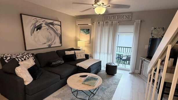 A living room with a dark sofa, a round coffee table, a ceiling fan, and a sign reading 'BEACH HOUSE.' - Stylish updated 2-bdrm/1.5 bath Condo across from Residents Beach Marco Island (Marco Island)