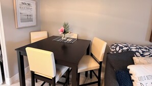 A dining area with a table and chairs, a framed picture on the wall, and a couch with a pillow. - Stylish updated 2-bdrm/1.5 bath Condo across from Residents Beach Marco Island (Marco Island)