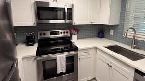 A modern kitchen with white cabinets, a stainless steel refrigerator, a microwave, a stove, and a sink. - Stylish updated 2-bdrm/1.5 bath Condo across from Residents Beach Marco Island (Marco Island)