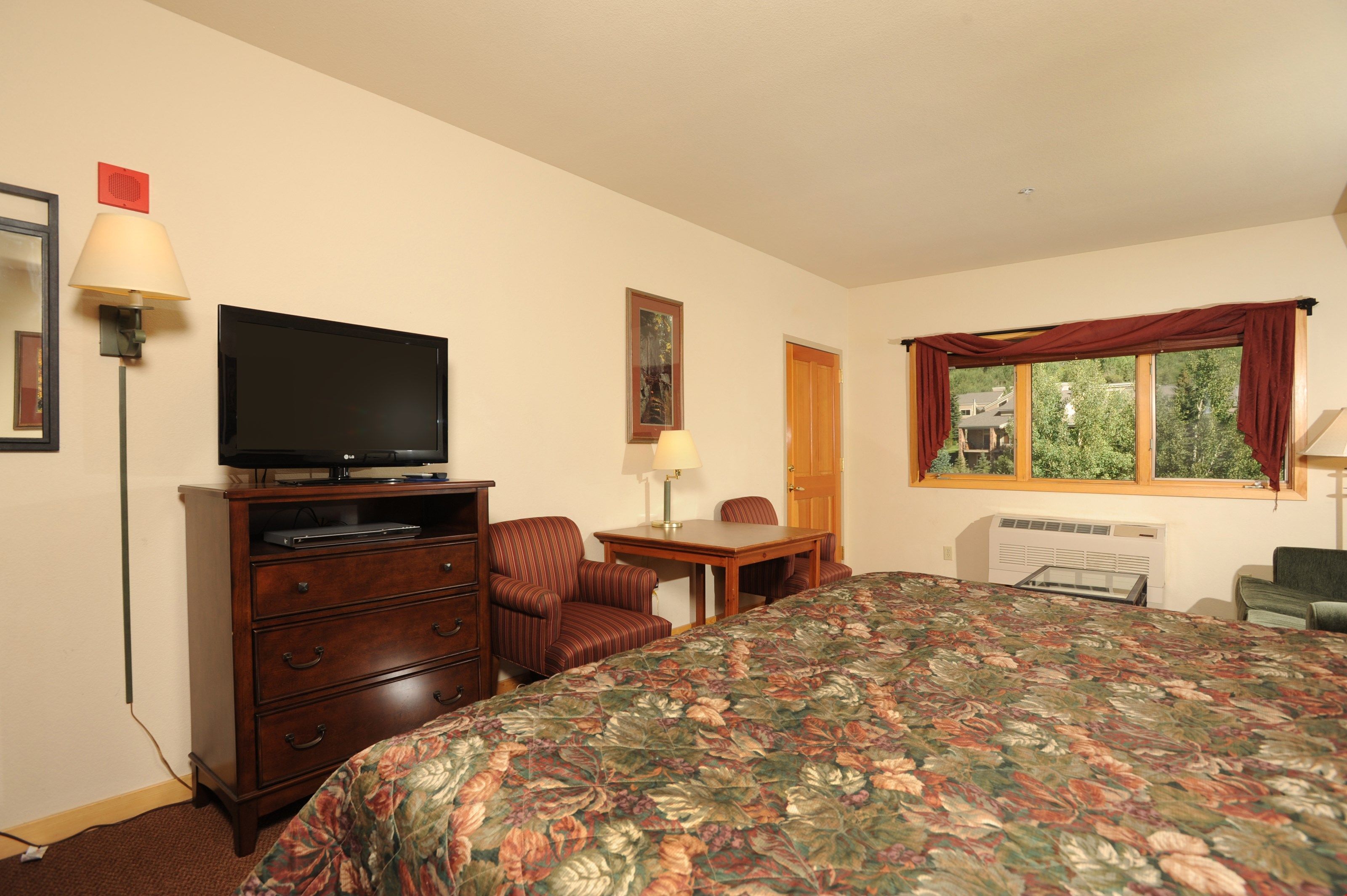 Una habitación de hotel con una cama grande, un televisor sobre un aparador de madera, un escritorio con una silla y una ventana con cortinas.