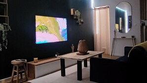 A modern living room with a flat-screen TV, wooden flooring, a sofa, a coffee table, and a small stool. - L'oasis Noir, comfortable 50m2 apartment (Calonne-Ricouart)