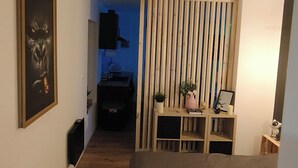 A narrow hallway leading to a bedroom with a bed, a wooden partition, a small table with a plant, and a framed picture on the wall. - L'oasis Noir, comfortable 50m2 apartment (Calonne-Ricouart)