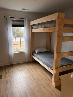 Habitación con literas, ventana, suelo de madera y una mesita.