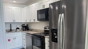 Una cucina moderna con mobili bianchi, elettrodomestici in acciaio inossidabile, un forno a microonde, un forno e un frigorifero.