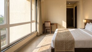 A hotel room with a large window, a bed, a desk, and a chair. - Barak Glow Stay (Silchar)