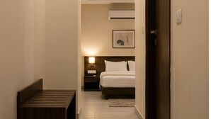 A narrow hallway leading to a bedroom with a bed, bedside table, and wall-mounted air conditioning unit. - Barak Glow Stay (Silchar)