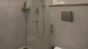 A modern bathroom with a glass-enclosed shower, a toilet, and a shelf with toiletries. - Barak Glow Stay (Silchar)
