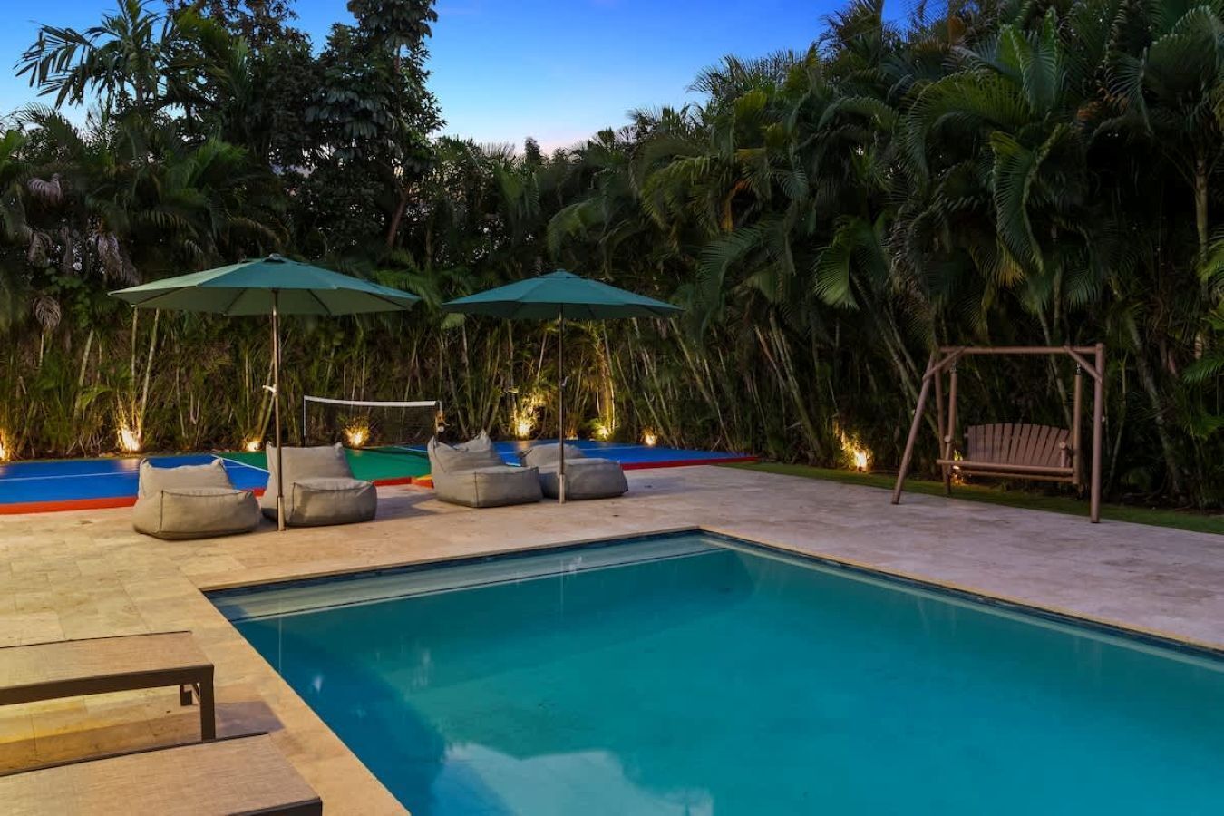 Piscina con sillas de descanso y sombrillas, rodeada de exuberante follaje tropical.