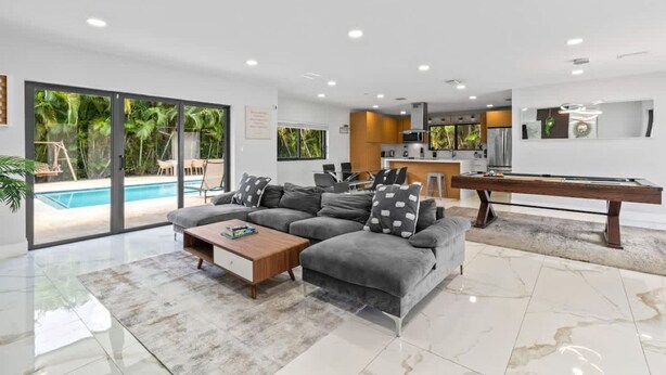 Ein modernes Wohnzimmer mit Pool, grauem Sofa, Couchtisch und Billardtisch.
