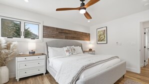 Une chambre à coucher avec un lit, des tables de chevet, un ventilateur de plafond, une fenêtre et une porte.