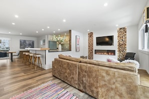 A modern living room with a sofa, a TV mounted on the wall, and a fireplace. - The Alpine Atelier I 4BR Townhome Near Shuttle Stop (Vail)