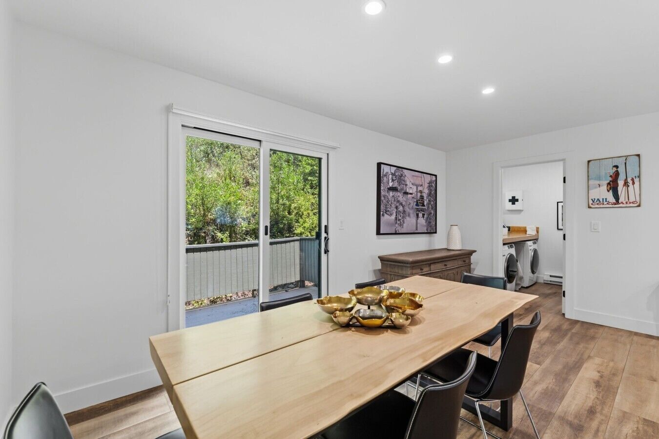 A modern kitchen with a wooden table, chairs, and a view through the glass door.