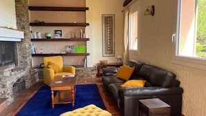 Una sala de estar con chimenea, un sofá, un sillón amarillo y una mesa de centro.