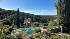 Piscina con barandilla blanca, rodeada de follaje y con vistas a un valle boscoso.