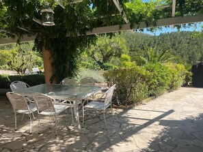 An outdoor patio with a table and chairs, surrounded by greenery and a pergola. - Villa Rhea - Pool - Panoramic Views of the Sea and Hills (La Londe-les-Maures)