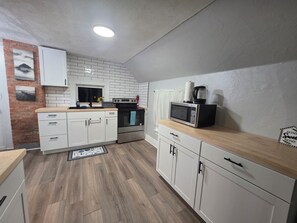 Eine moderne Küche mit weißen Schränken, einer Ziegelwand als Blickfang, einem Edelstahlbackofen und einer Mikrowelle auf der Arbeitsfläche.