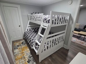 Una cama litera con una colcha estampada, una puerta, un tapete con diseño y un sofá con almohadas en la habitación contigua.