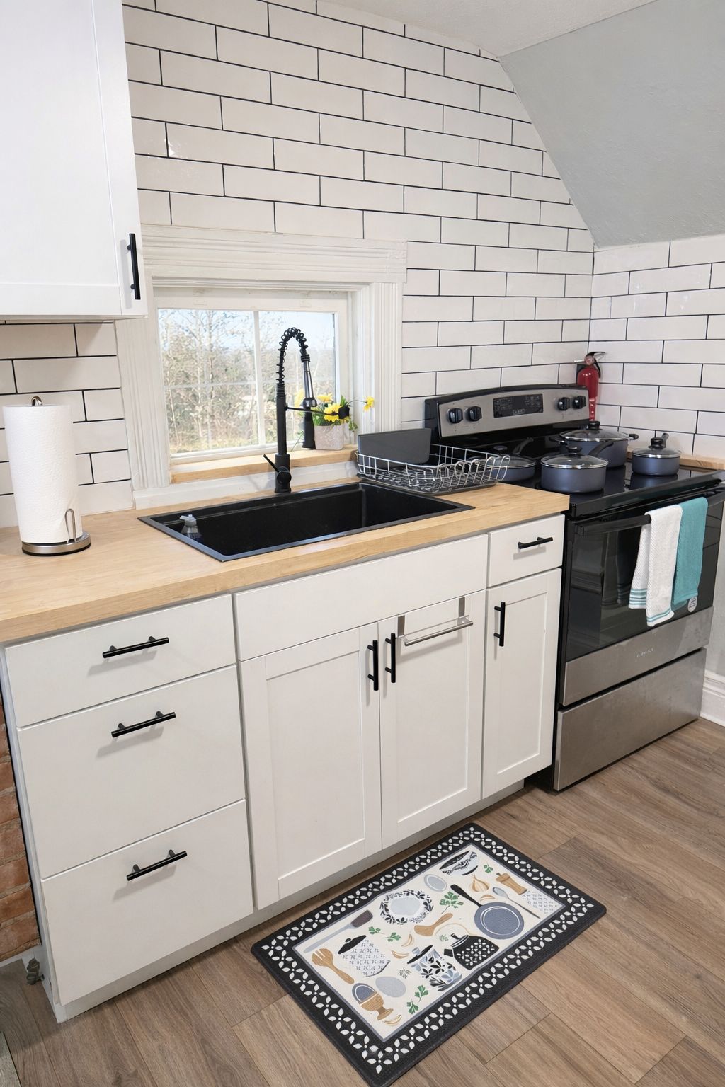A kitchen with white cabinets, a black stove, and a window with a view of trees.