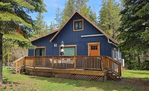A blue cabin with a wooden deck, a front door, and a window.