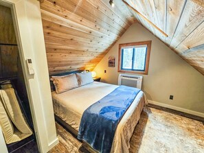 Une chambre avec un plafond en pente, un lit, une table de chevet, une fenêtre et un radiateur.