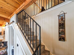 Un escalier avec une rampe en métal noir, des poutres en bois et une œuvre d’art sur le thème des animaux fixée au mur.