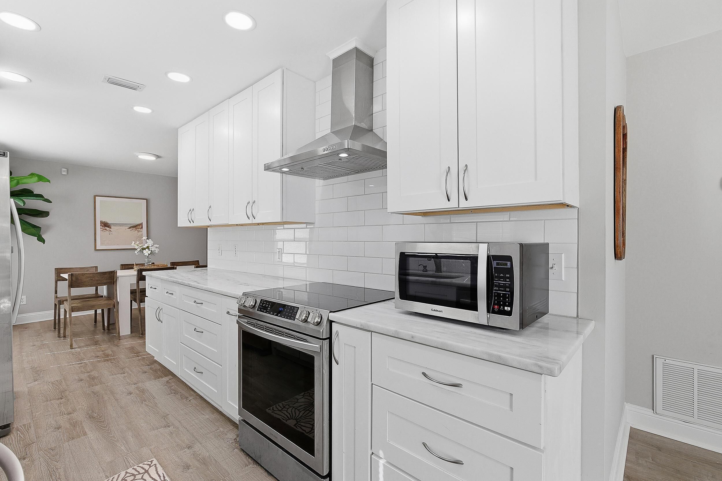 A modern kitchen with white cabinets, a stainless steel range hood, a built-in oven, and a microwave.