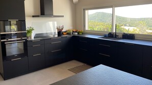 Une cuisine moderne avec des meubles de couleur noire, un four encastré et une fenêtre donnant sur un paysage montagneux.